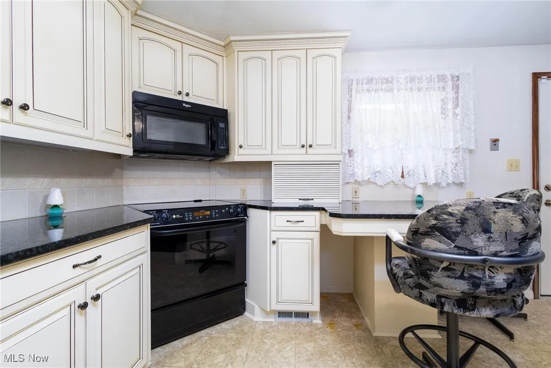 Kitchen featuring black appliances, dark stone counters, cream cabinets, and decorative backsplash