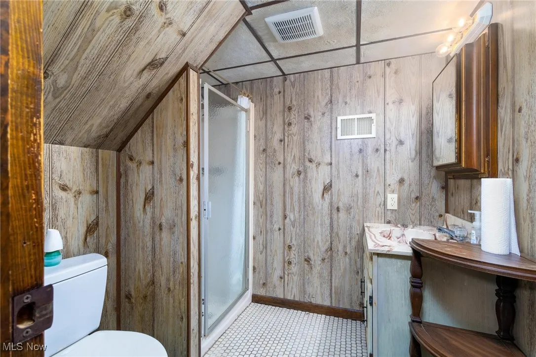Full bathroom featuring vanity, a stall shower, and wood walls