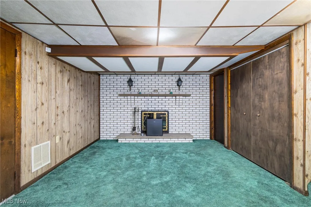 Unfurnished living room with wooden walls, carpet floors, a brick fireplace, and a drop ceiling