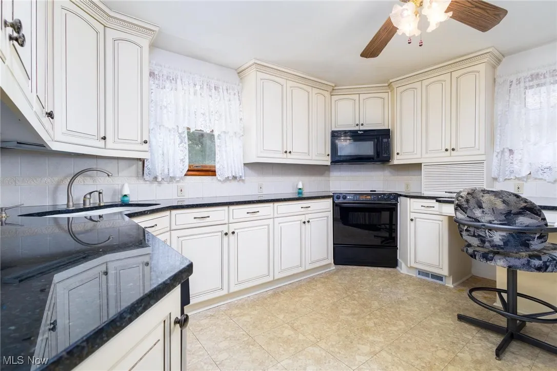 Kitchen with black appliances, cream cabinetry, dark stone countertops, tasteful backsplash, and light flooring