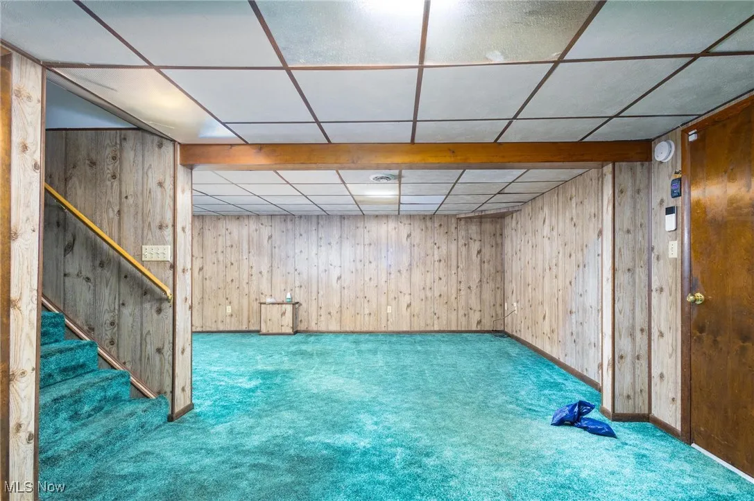Finished below grade area featuring wooden walls, carpet floors, a paneled ceiling, and stairway