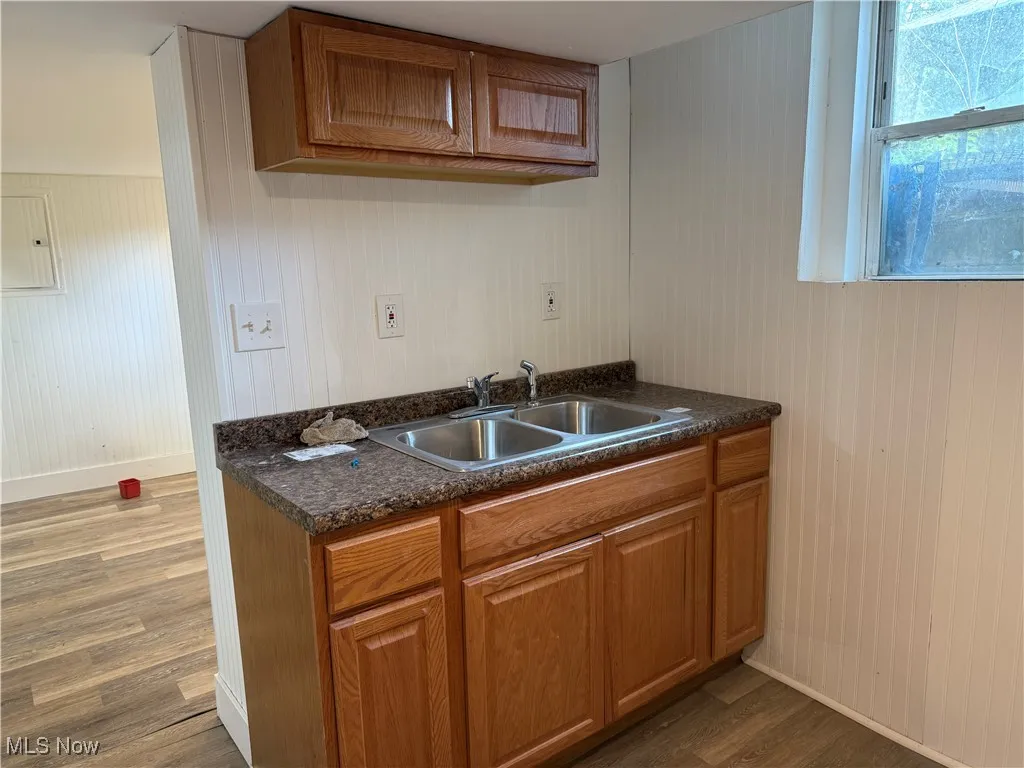 Kitchen featuring brown cabinetry, dark countertops, dark wood-type flooring, electric panel, and wood walls