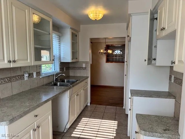 Kitchen with glass insert cabinets, decorative backsplash, a chandelier, light tile patterned floors, and white cabinets