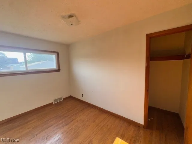 Unfurnished bedroom with wood finished floors and a spacious closet