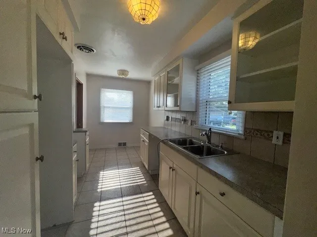 Kitchen with light tile patterned floors, backsplash, glass insert cabinets, and white cabinets