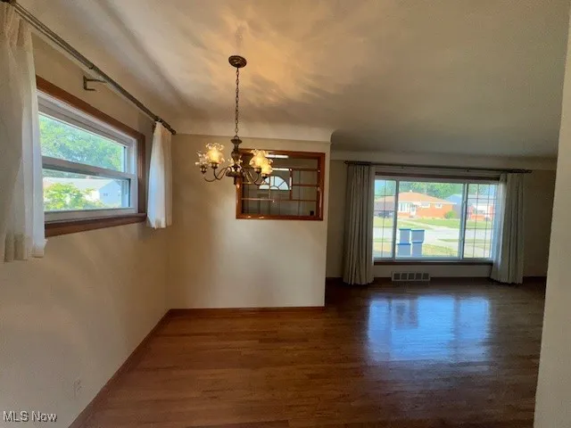 Unfurnished dining area with dark wood-style flooring and a chandelier