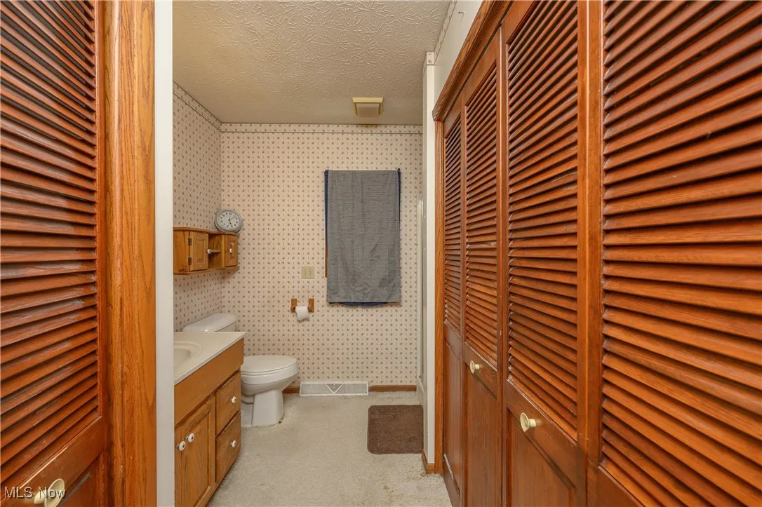 Bathroom with a closet, vanity, a textured ceiling, and wallpapered walls