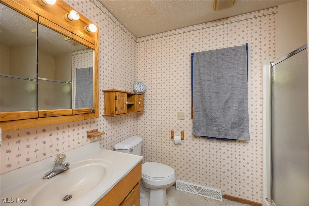 Full bath featuring a textured ceiling, vanity, a shower stall, and wallpapered walls