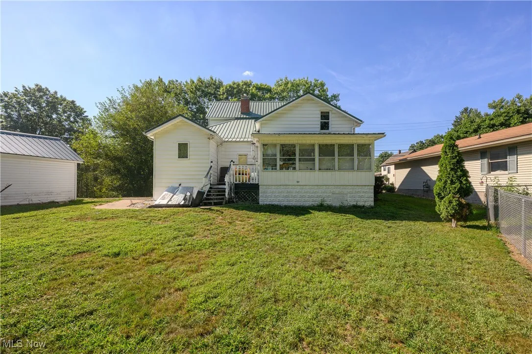 Back of property with a sunroom, a lawn, a chimney, a deck, and a metal roof