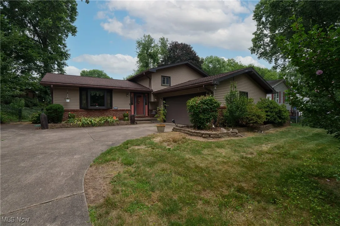 Split level home featuring a garage, a front yard, brick siding, and driveway