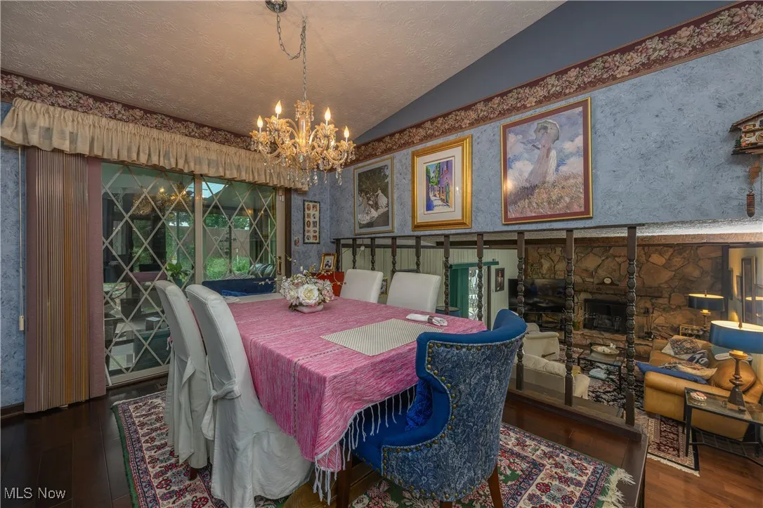 Dining area featuring wallpapered walls, vaulted ceiling, wood finished floors, a textured ceiling, and a chandelier