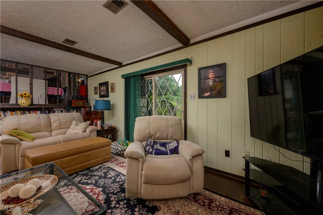 Living room featuring beam ceiling, wood finished floors, wood walls, and a textured ceiling