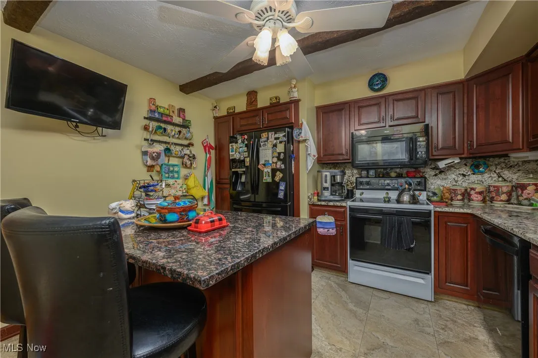 Kitchen with black appliances, dark stone countertops, a breakfast bar area, decorative backsplash, and beam ceiling
