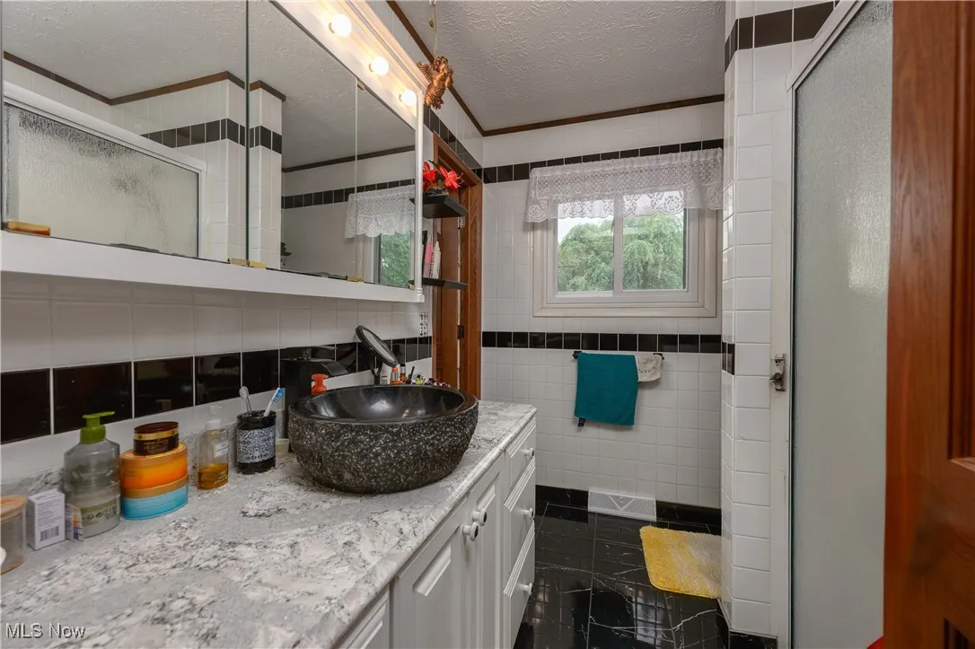 Full bathroom featuring tile walls, a shower stall, vanity, a textured ceiling, and ornamental molding