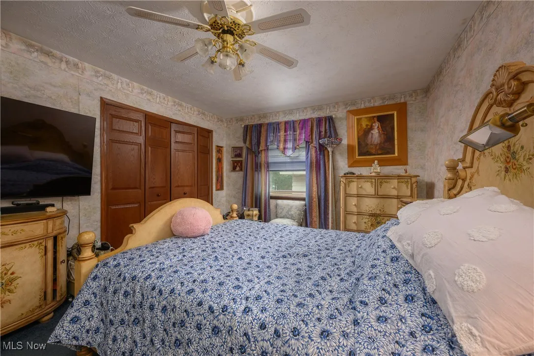 Bedroom with wallpapered walls, ceiling fan, a closet, and a textured ceiling