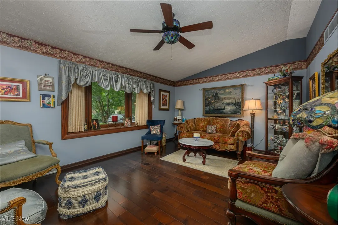 Living area with a textured ceiling, vaulted ceiling, ceiling fan, and wood-type flooring