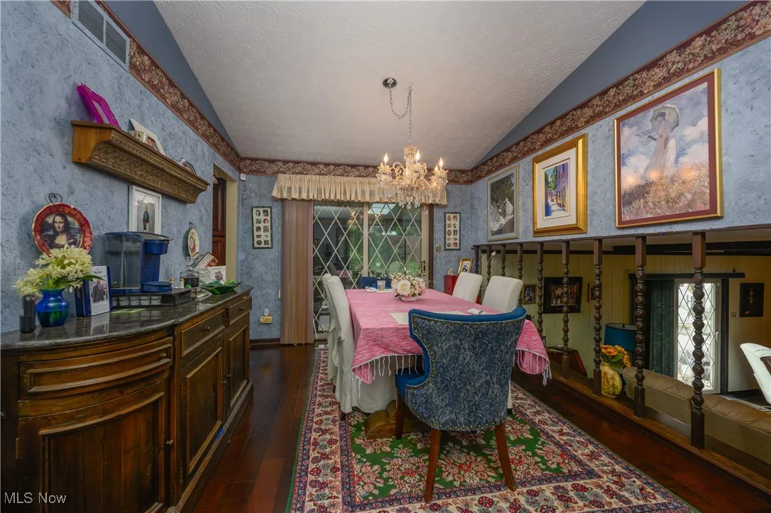 Dining area with a chandelier, dark wood-style floors, lofted ceiling, wallpapered walls, and a textured ceiling
