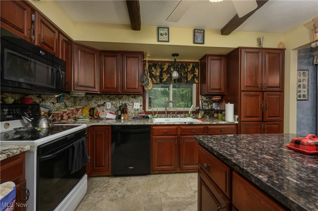 Kitchen with beamed ceiling, black appliances, dark stone counters, a textured ceiling, and backsplash