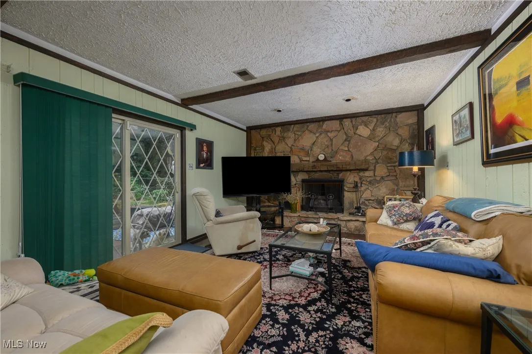 Living area featuring wood walls, a stone fireplace, a textured ceiling, and beam ceiling