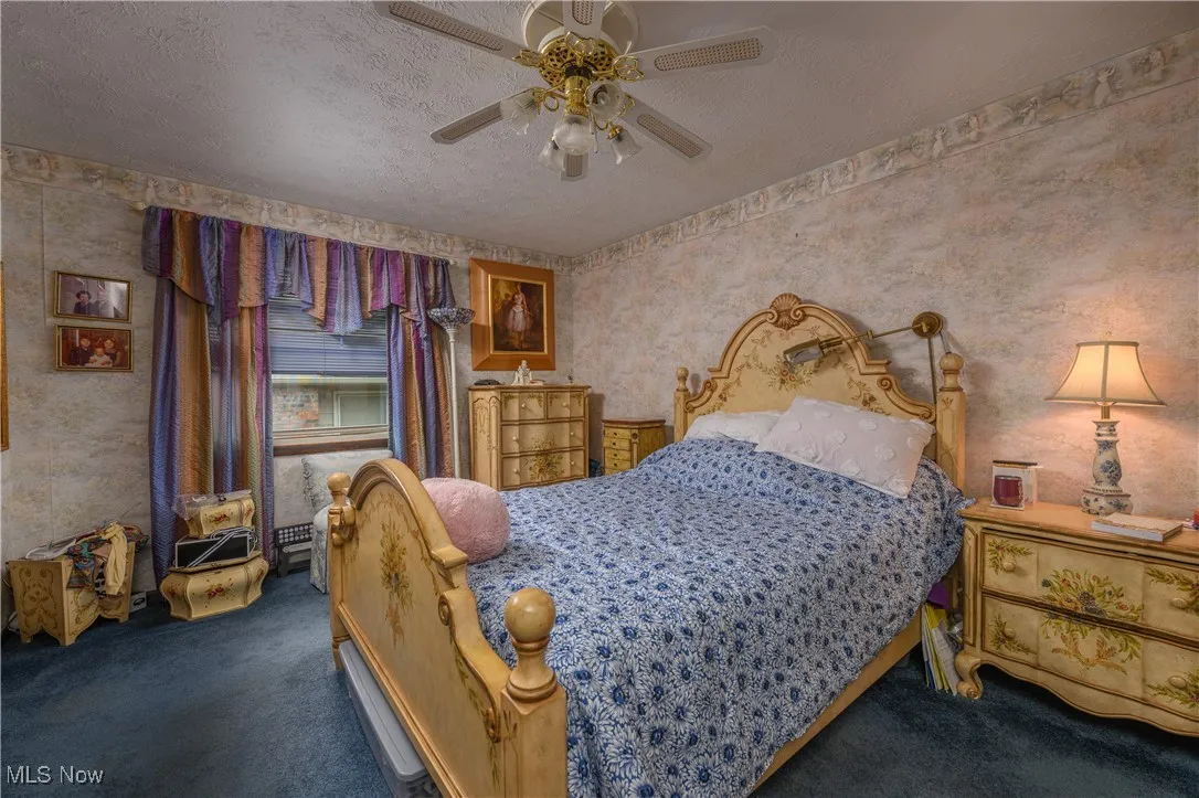 Carpeted bedroom with a textured ceiling, ceiling fan, and wallpapered walls
