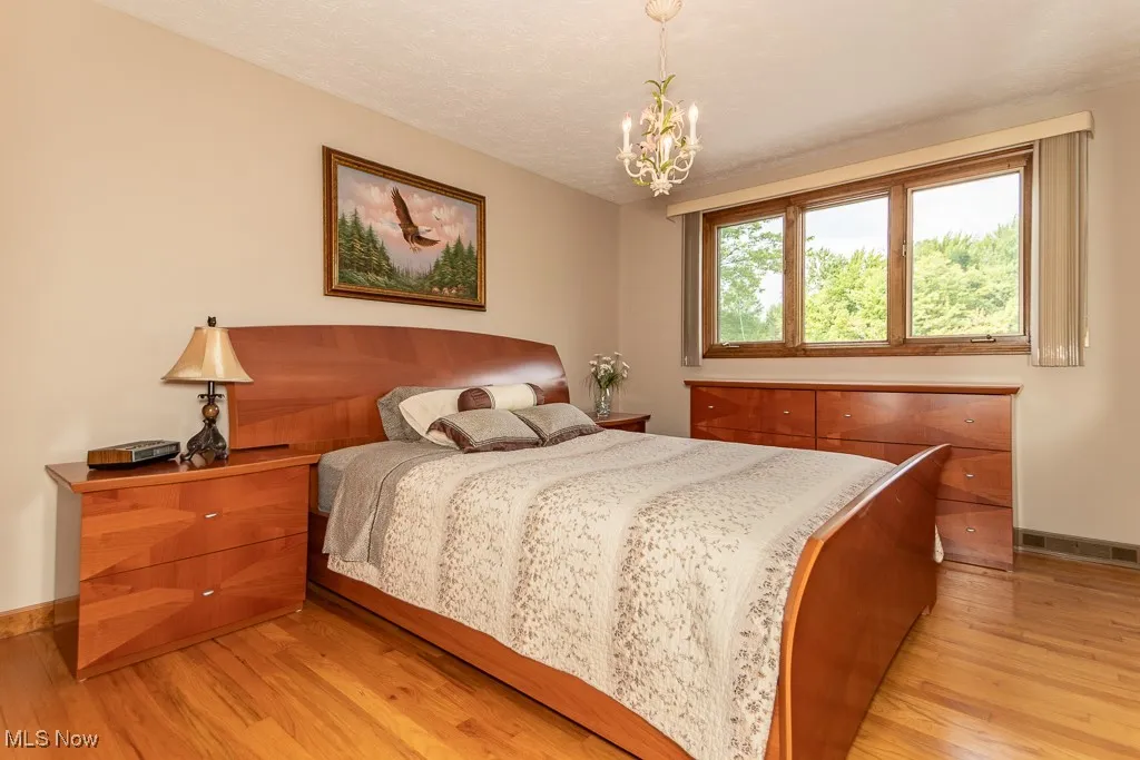 Bedroom featuring light woodflooring, a chandelier, and a textured ceiling