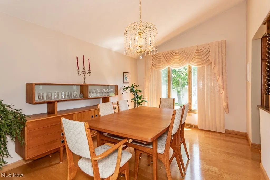 Dining space featuring light wood flooring, vaulted ceiling, and a chandelier