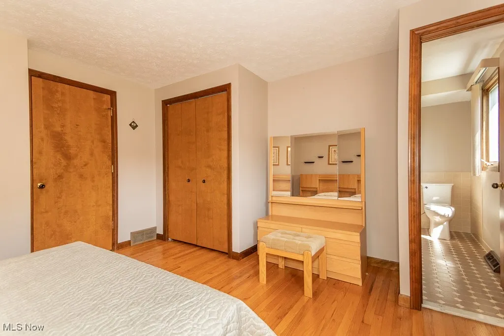 Bedroom featuring a textured ceiling, light wood-style floors, a closet, and ensuite bathroom