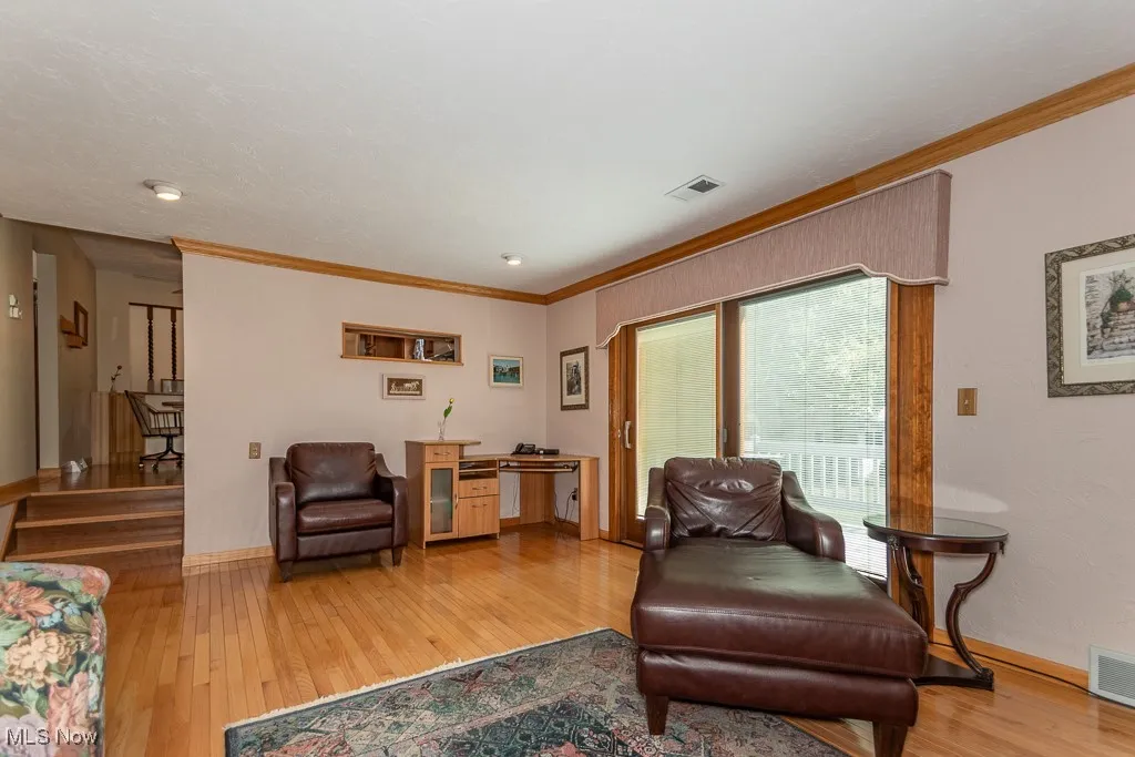 Living area featuring light wood-style flooring, crown molding, and stairway