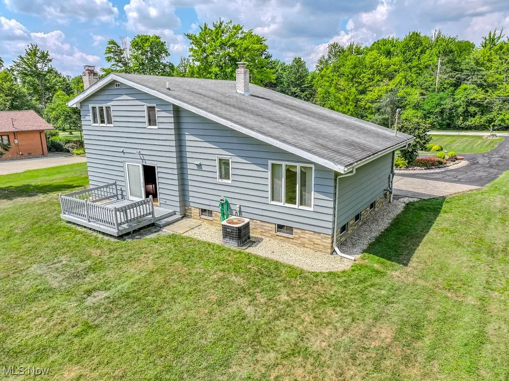 Rear view of house featuring a chimney, a lawn, a deck, and roof with shingles