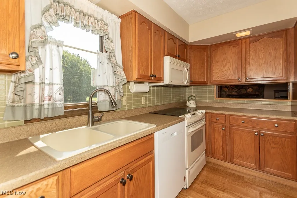 Kitchen featuring brown cabinets, backsplash, white appliances, and light wood finished floors