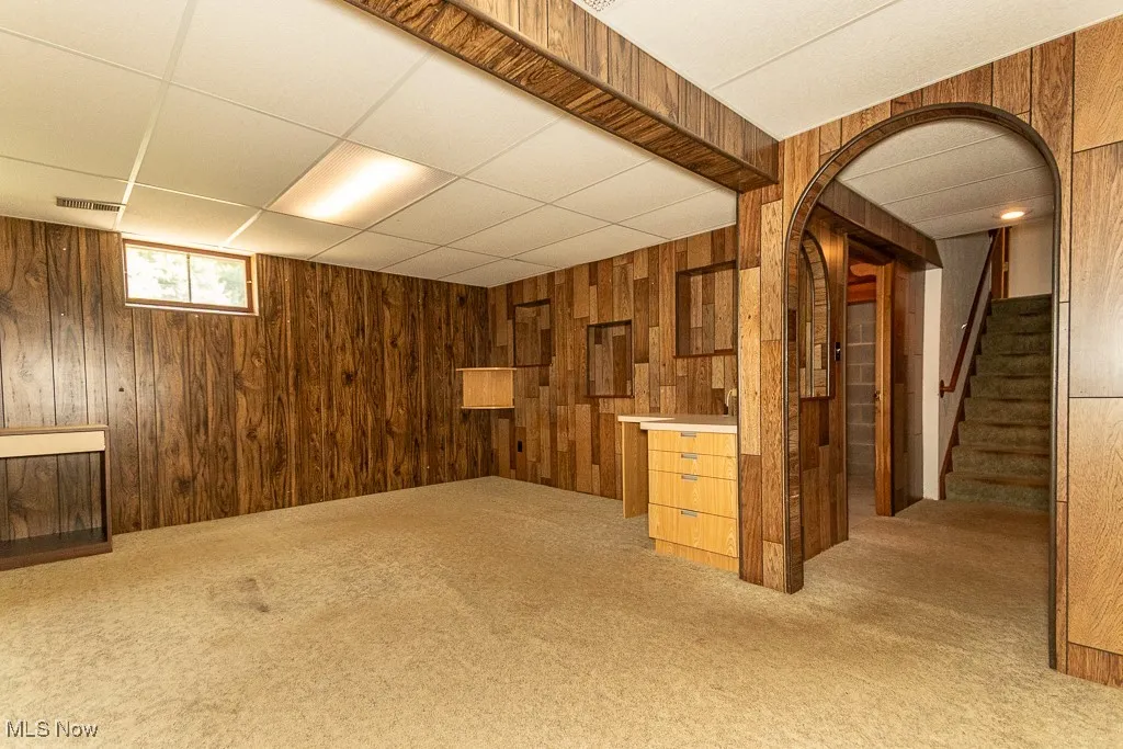 Below grade area featuring wood walls, a paneled ceiling, light carpet, and stairs