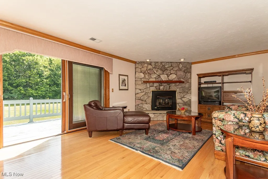 Living area featuring crown molding, light wood finished floors, and a stone fireplace