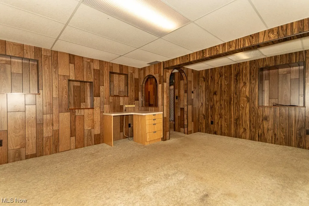 Below grade area with a drop ceiling, light colored carpet, wooden walls, and arched walkways