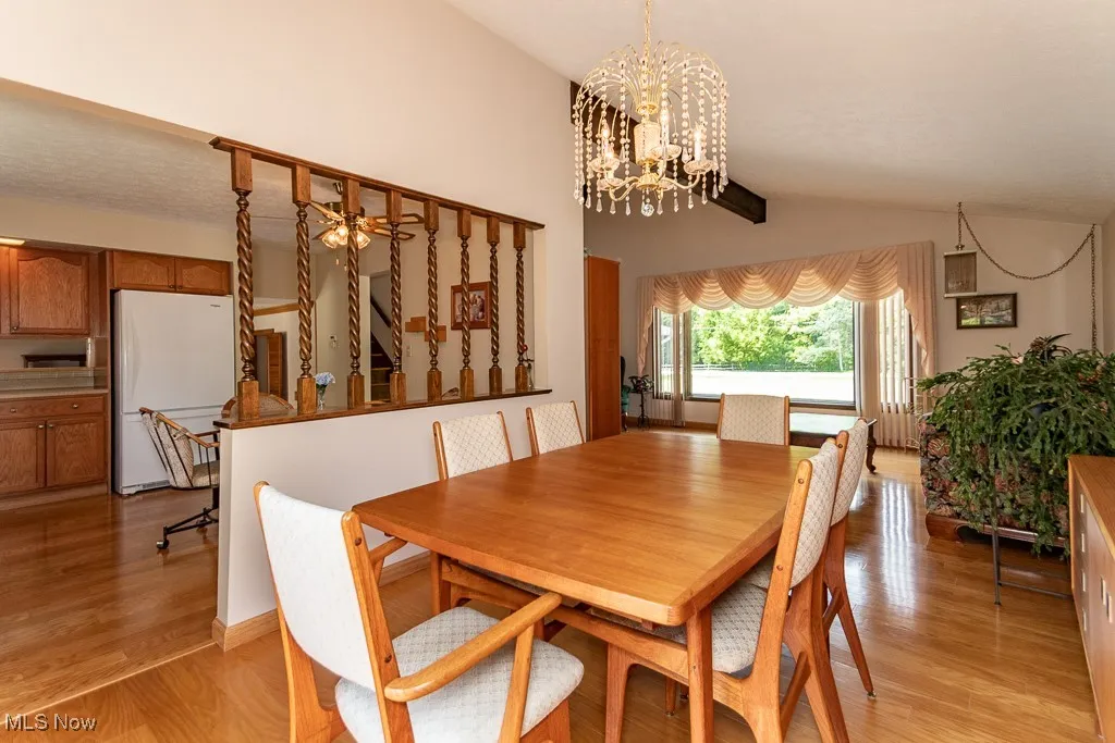 Dining area with light wood flooring, ceiling fan, vaulted ceiling, and a chandelier