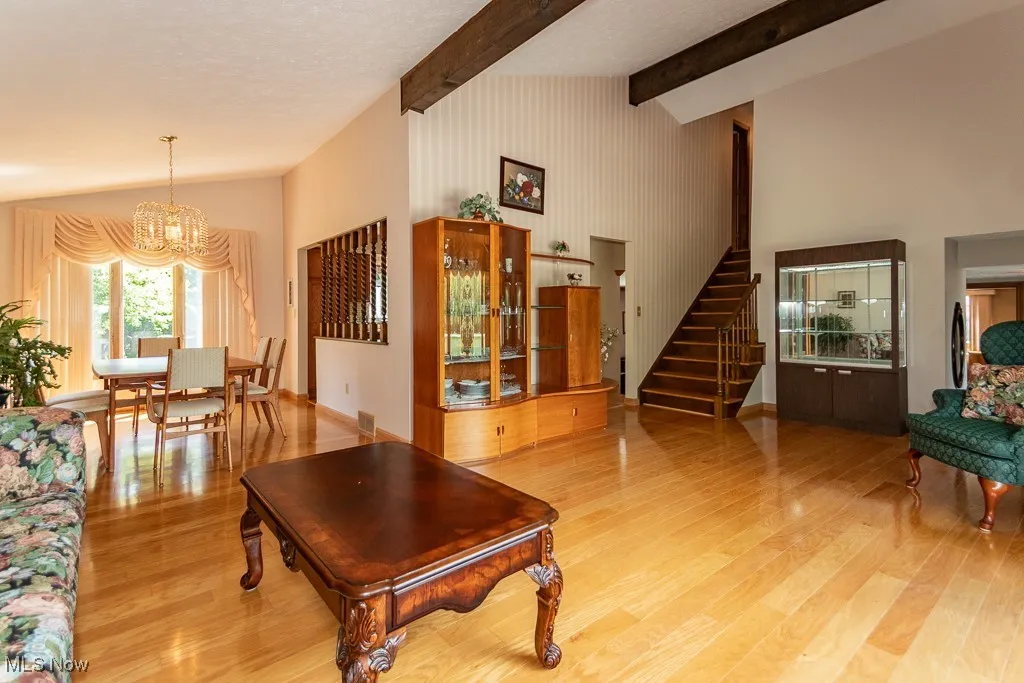 Living room with stairs, high vaulted ceiling, a chandelier, light wood-style flooring, and beam ceiling