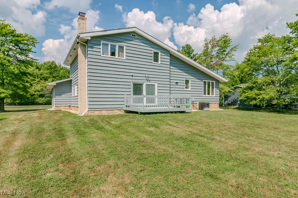 Rear view of house featuring a lawn, a chimney, and a wooden deck