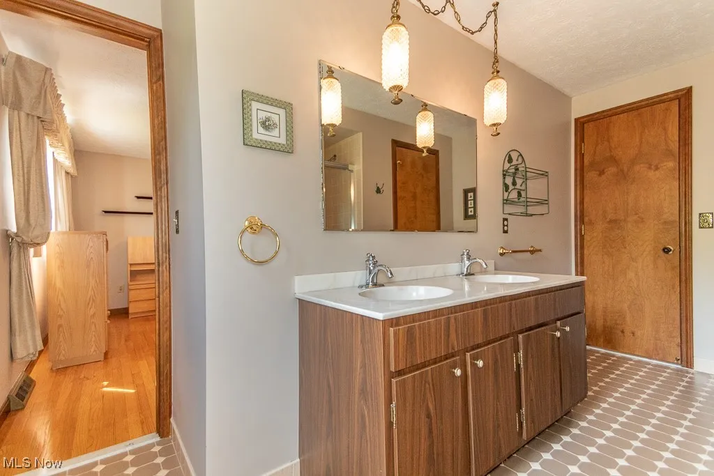 Bathroom featuring double vanity, a textured ceiling, and a shower with shower door