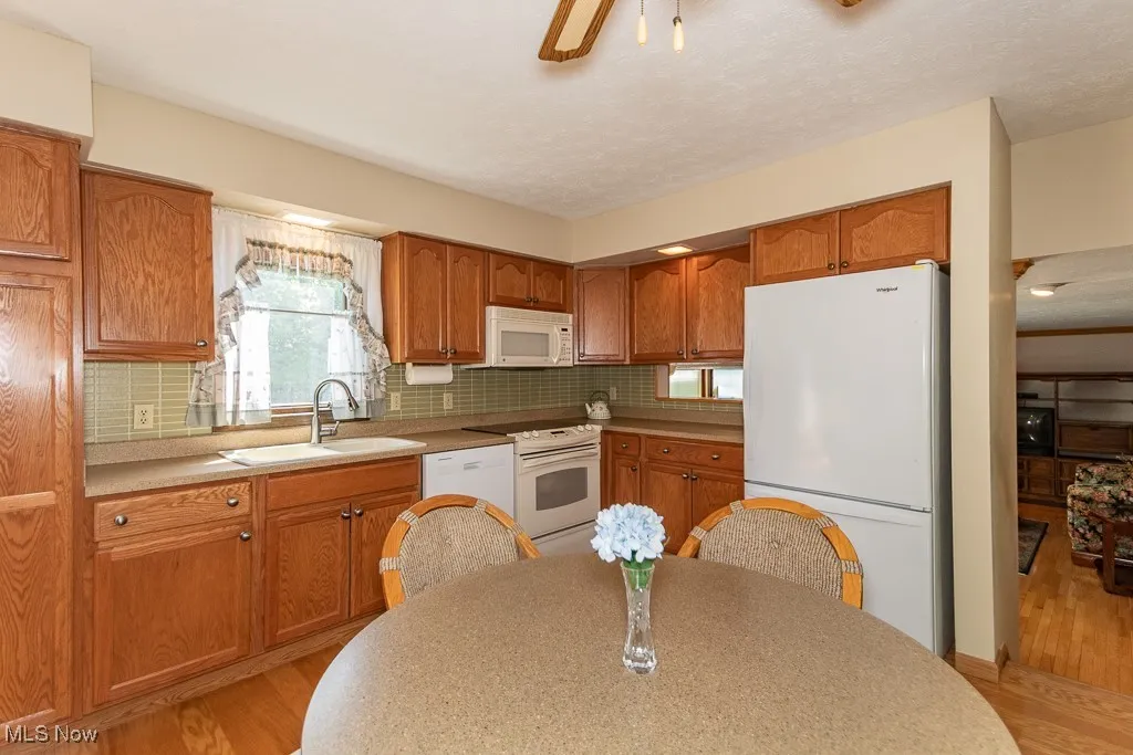 Kitchen with light wood-type flooring, white appliances, brown cabinets, backsplash, and a textured ceiling