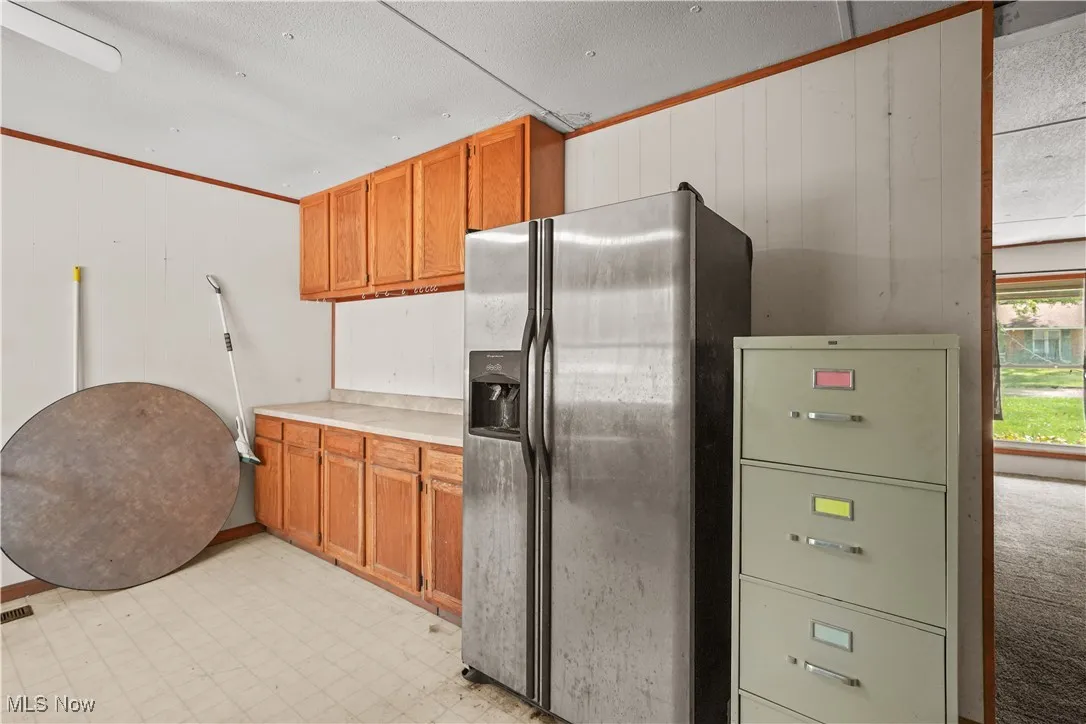 Kitchen featuring stainless steel refrigerator with ice dispenser, light countertops, crown molding, brown cabinets, and light floors
