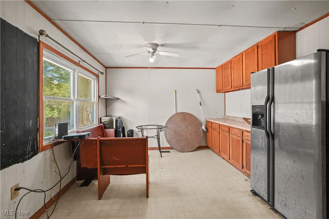 Kitchen with stainless steel fridge, light countertops, crown molding, brown cabinetry, and ceiling fan