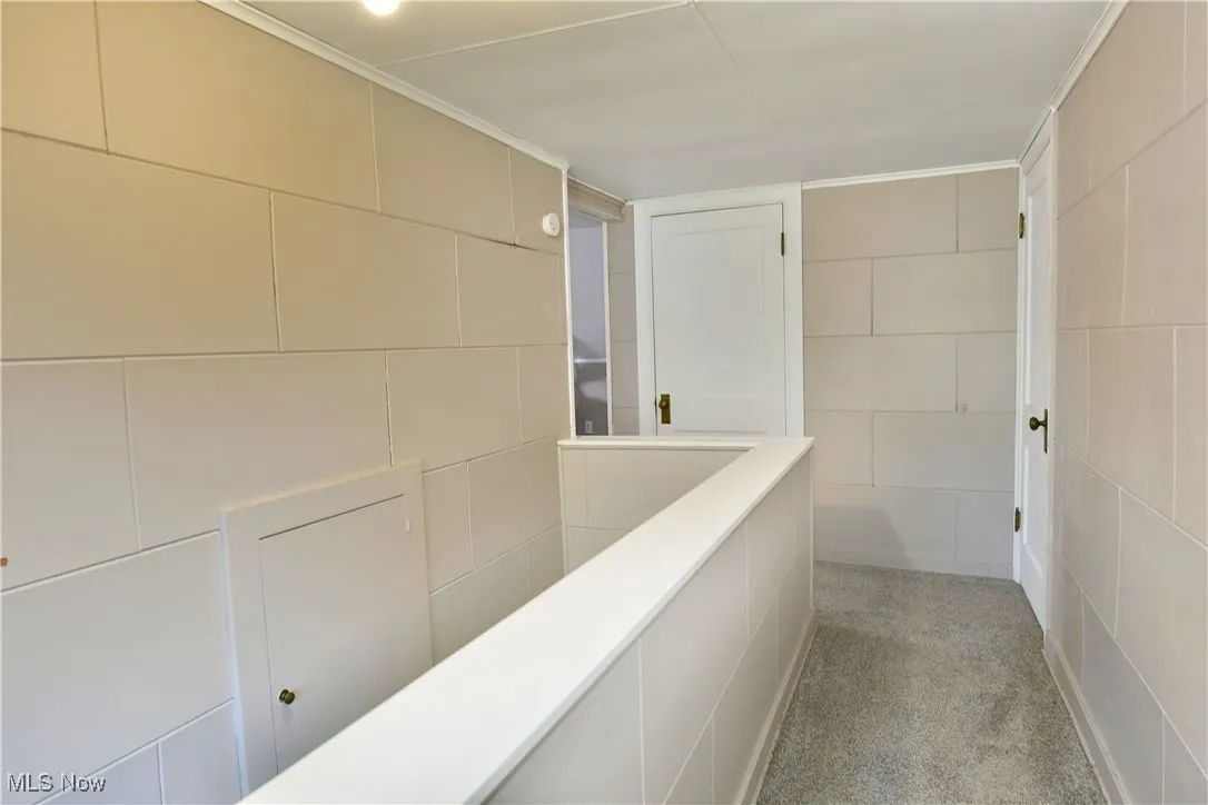 Hall with light colored carpet, crown molding, and tile walls