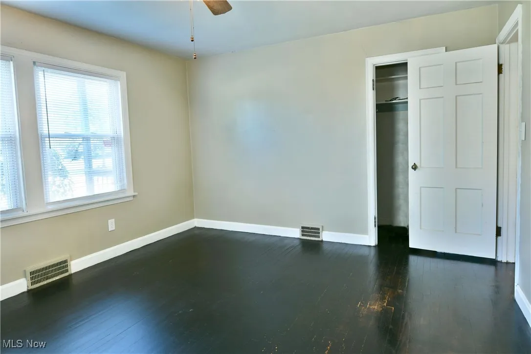Unfurnished bedroom featuring dark wood-type flooring, a closet, and a ceiling fan