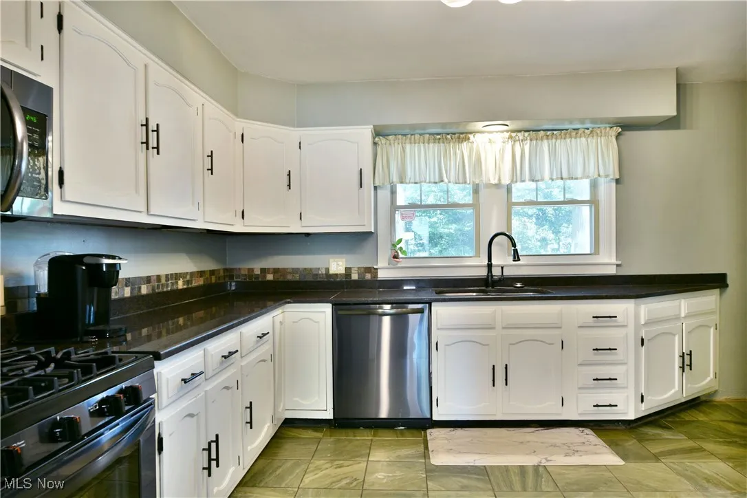 Kitchen featuring white cabinetry, dishwasher, range with gas cooktop, black microwave, and dark stone counters