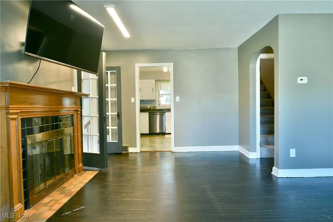 Unfurnished living room featuring dark wood-style floors, arched walkways, a tile fireplace, and stairway