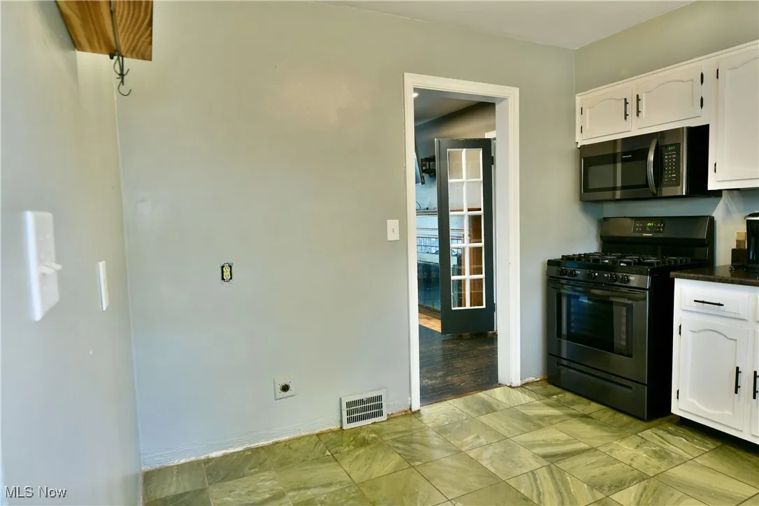 Kitchen with white cabinets, black gas stove, stainless steel microwave, and dark stone counters
