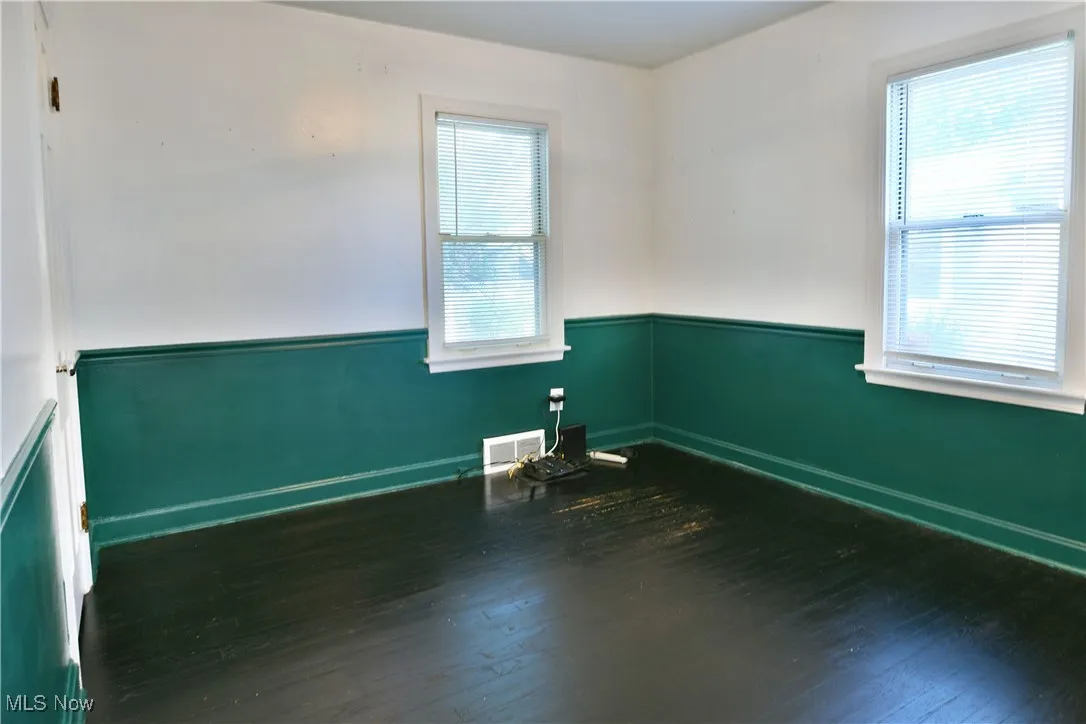 Unfurnished room with dark wood-style flooring and wainscoting