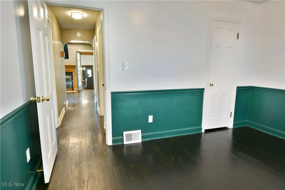 Unfurnished room with arched walkways, dark wood-type flooring, and wainscoting