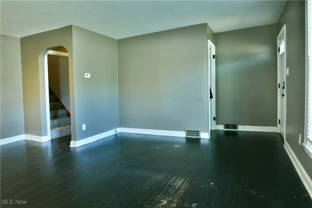 Unfurnished room featuring stairs, dark wood-style flooring, and arched walkways