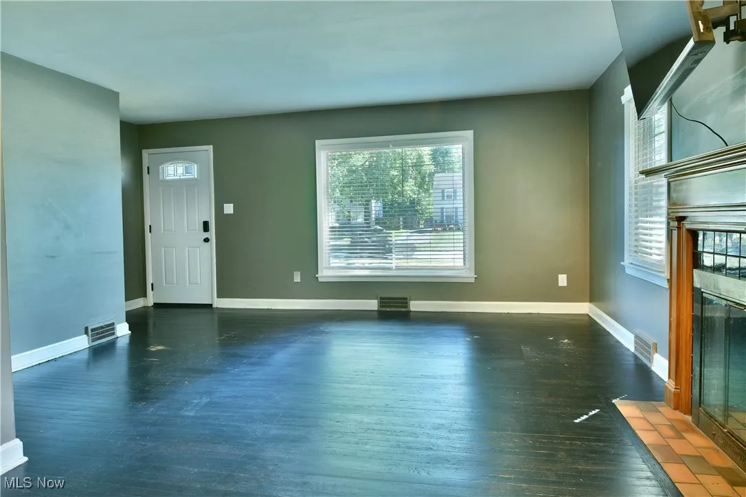 Unfurnished living room with a tile fireplace, dark wood-style flooring, and healthy amount of natural light