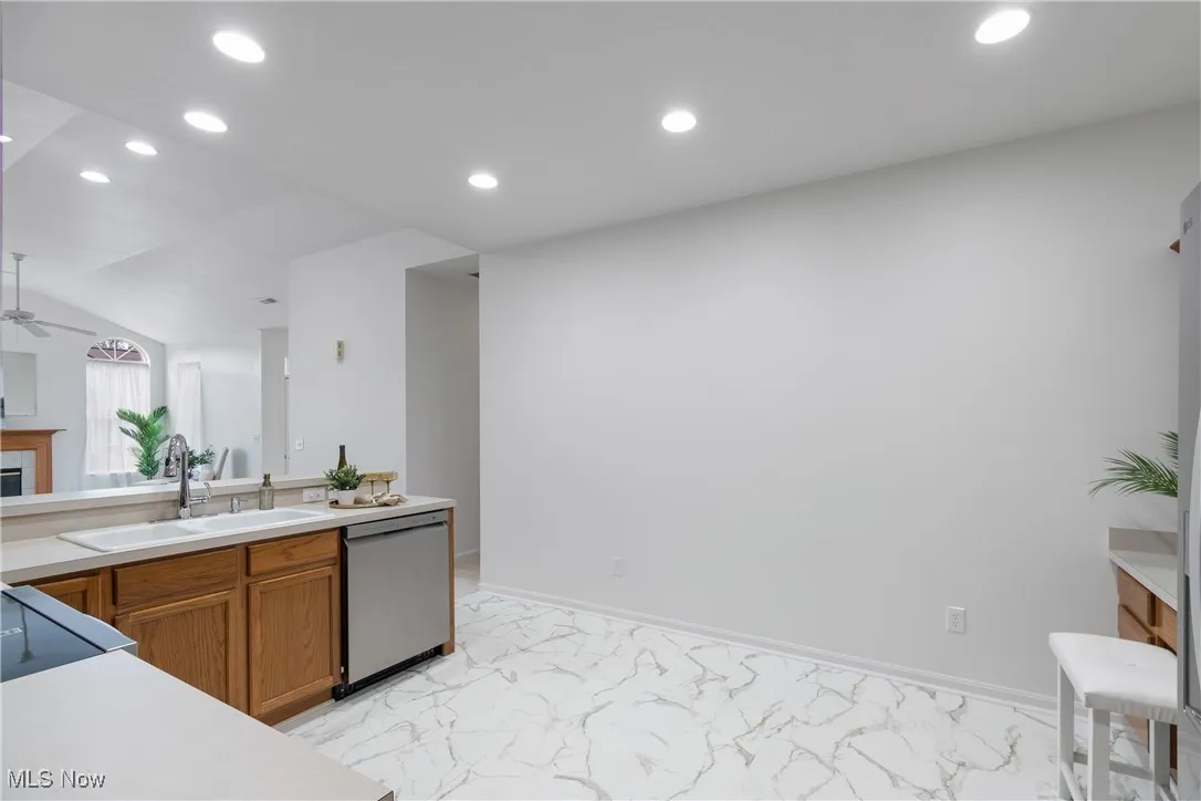 Kitchen featuring brown cabinets, light countertops, recessed lighting, stainless steel dishwasher, and light marble finish floors